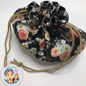 May include: A black drawstring bag with a floral print featuring pink, white, and yellow roses. The bag has a tan drawstring and is made of fabric.