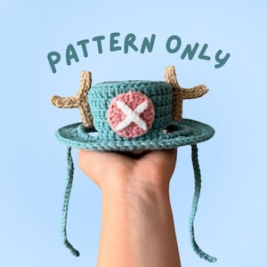 Könnte beinhalten: Gehäkelter Hut in Türkis, Beige und Rosa mit breiter Krempe und zwei kreuzförmigen Akzenten in Beige. Er hat ein rundes Emblem mit weißem Kreuz auf rosa Grund. Der Text "PATTERN ONLY" befindet sich über dem Hut.