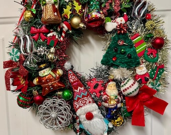 Puede incluir: Una corona navideña festiva con una variedad de adornos. La corona presenta un gnomo, figuras de Papá Noel, bastones de caramelo y lazos rojos. La corona está decorada con detalles verdes, rojos, dorados y plateados.