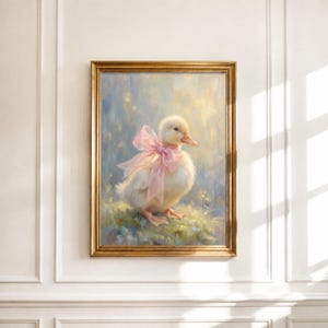 May include: A framed oil painting depicting a fluffy yellow duckling standing in a soft-focus field. The duckling wears a large, translucent pink ribbon tied around its neck. The artwork is enclosed in a metallic gold frame with a classic profile.