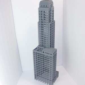 May include: A gray 3D printed model of a tall skyscraper building with many windows. The model is detailed and realistic, with a flat roof and a base.