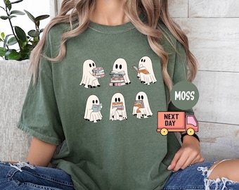 May include: A green t-shirt with a graphic of five ghosts reading books. The text "Moss Next Day" is visible on a pink truck sticker on the shirt.