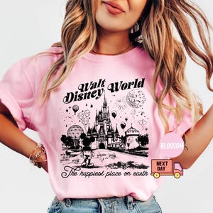 May include: Pink t-shirt with a black and white graphic of the Walt Disney World castle, Mickey Mouse, and the text "Walt Disney World" and "The happiest place on earth". The shirt has short sleeves.