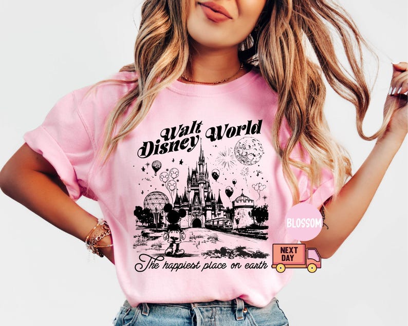 May include: Pink t-shirt with a black and white graphic of the Walt Disney World castle, Mickey Mouse, and the text "Walt Disney World" and "The happiest place on earth". The shirt has short sleeves.