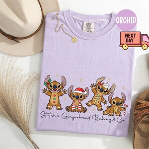 Puede incluir: Una camiseta de color lila claro con un dise&ntilde;o de Stitch con tem&aacute;tica de pan de jengibre. El gr&aacute;fico incluye cuatro personajes de Stitch vestidos como hombres de jengibre, con el texto "Stitch's Gingerbread Baking & Co." debajo. Tambi&eacute;n se ve un collar dorado y sandalias.