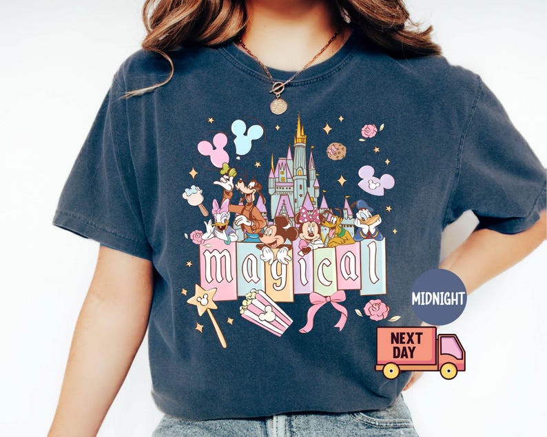 May include: Dark blue t-shirt featuring a colorful graphic with Disney characters, a castle, and the word "magical". The design includes Mickey Mouse, Donald Duck, and other characters, with stars and flowers. A magic wand and popcorn are also included.