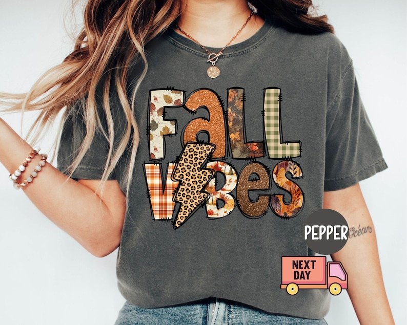 May include: A grey t-shirt with a patchwork design that says "Fall Vibes". The design features a lightning bolt with a leopard print, plaid, and autumn leaves.