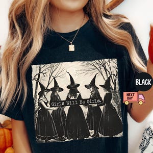 May include: Black t-shirt with a vintage illustration of four witches in black dresses and pointed hats. The text "Girls Will Be Girls." is printed on the shirt.