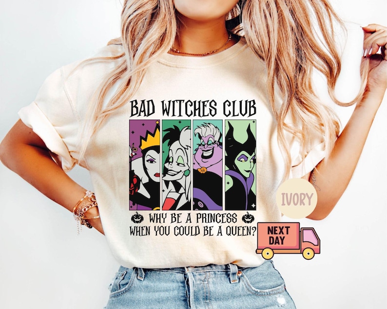 May include: Ivory-colored t-shirt featuring the text "BAD WITCHES CLUB" above four cartoon villain portraits. Below, the shirt reads "WHY BE A PRINCESS WHEN YOU COULD BE A QUEEN?" A small pumpkin graphic is on either side of the text.