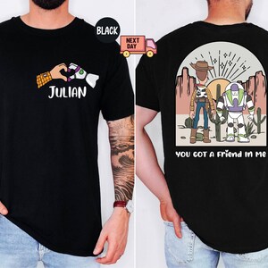 Pu&ograve; includere: Una t-shirt nera con una grafica frontale che mostra una mano umana e una mano robotica che formano un cuore sopra il nome JULIAN. La grafica sul retro mostra un cowboy e un ranger spaziale in un deserto con il testo YOU GOT A FRIEND IN ME.