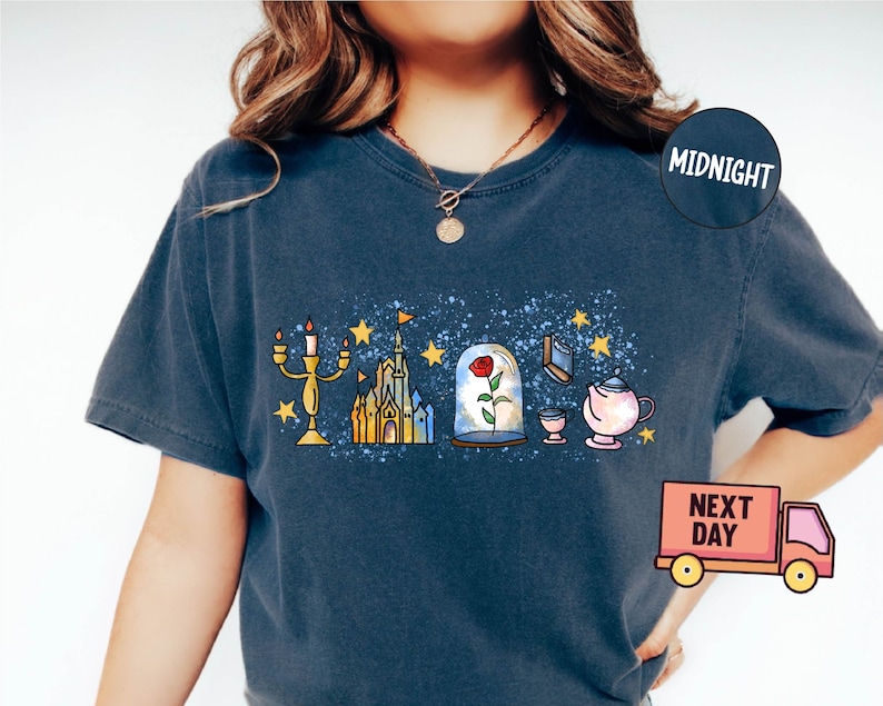 May include: A dark blue t-shirt with a white and yellow graphic print of a castle, a rose in a glass dome, a candlestick, a teacup, and a teapot. The graphic is on a blue background with white speckles. The shirt has a crew neck and short sleeves.
