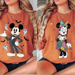 May include: Two orange t-shirts featuring Halloween-themed cartoon characters. One shirt displays Mickey Mouse as Jack Skellington, surrounded by bats and ghosts. The other shows Minnie Mouse in a patchwork dress with autumn leaves.