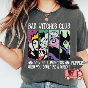 May include: Dark gray t-shirt with the text "BAD WITCHES CLUB" above four cartoon villain portraits. Below, the shirt reads "WHY BE A PRINCESS WHEN YOU COULD BE A QUEEN?" and features a pumpkin graphic.