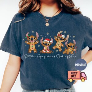 Puede incluir: Camiseta azul marino con cuatro personajes de dibujos animados con forma de pan de jengibre. Los personajes est&aacute;n decorados con detalles festivos como un gorro de Pap&aacute; Noel y un bast&oacute;n de caramelo. El texto "Stitch's Gingerbread Baking & Co" est&aacute; escrito en blanco.