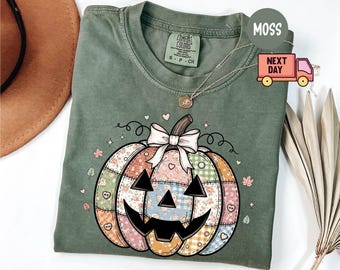 May include: A moss green Comfort Colors t-shirt featuring a patchwork pumpkin design with a smiling jack-o'-lantern face, a pink bow, and floral and heart accents. The shirt has a crew neck and short sleeves, perfect for fall.