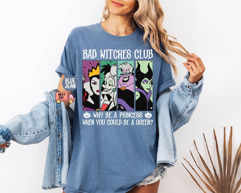 May include: A blue t-shirt with the text "BAD WITCHES CLUB" and the phrase "WHY BE A PRINCESS WHEN YOU COULD BE A QUEEN?" The shirt features four cartoon images of Disney villains. The shirt is a light blue color.