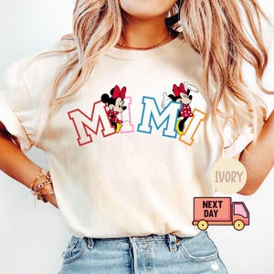 May include: A white t-shirt with the word "MIMI" in colorful letters and a cartoon image of Mickey Mouse's girlfriend Minnie Mouse on each side of the word.