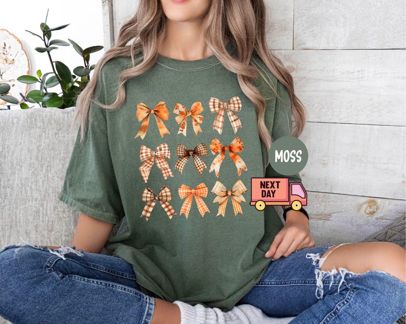 May include: A green t-shirt with a pattern of orange and brown bows. The shirt has a crew neck and short sleeves. The text "Moss Next Day" is printed on the shirt.