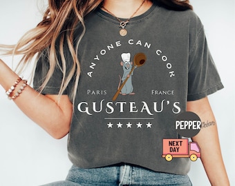 May include: A dark grey t-shirt with the text "Anyone Can Cook" and a cartoon rat chef holding a spoon. The text "Paris Gusteau's France" is below the rat chef. Five stars are below the text.