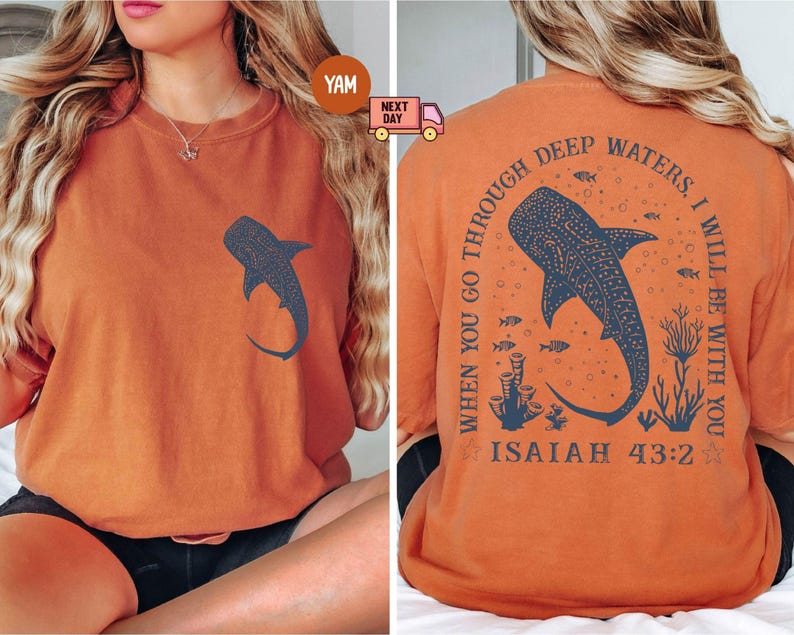 Op de afbeelding: Oranje T-shirt met een walvishaai-afbeelding op de voorkant en de tekst "WHEN YOU GO THROUGH DEEP WATERS I WILL BE WITH YOU ISAIAH 43:2" op de achterkant.