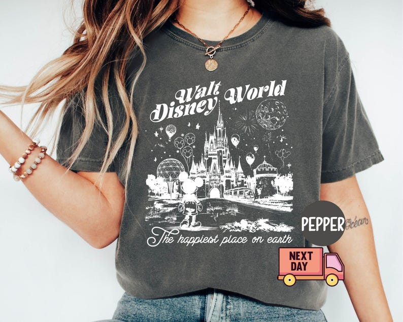 May include: Dark gray t-shirt featuring a white graphic of the Walt Disney World castle, Mickey Mouse, and fireworks. The text "Walt Disney World" and "The happiest place on earth" are also displayed. The shirt has a crew neck.