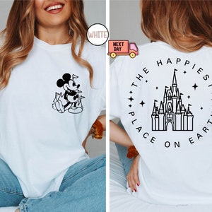K&ouml;nnte beinhalten: Wei&szlig;es T-Shirt mit einer Schwarzwei&szlig;illustration von Mickey Mouse auf der Vorderseite und dem Text "The Happiest Place on Earth" mit einer Schwarzwei&szlig;illustration von Schloss Aschenputtel auf der R&uuml;ckseite.