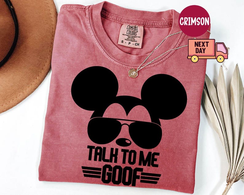 May include: A crimson short-sleeved t-shirt featuring a black graphic of a mouse silhouette wearing sunglasses. Below the graphic, the text reads TALK TO ME GOOF in bold black capital letters. The shirt has a crew neckline and a Comfort Colors label.