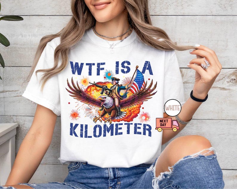 May include: White t-shirt with a graphic featuring an eagle carrying a person with a gun and an American flag. The text on the shirt reads "WTF IS A KILOMETER."