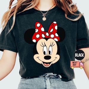 Może przedstawiać: Czarny T-shirt z grafiką Minnie Mouse w czerwonej kokardce w białe kropki. Koszulka ma postarzony wygląd.