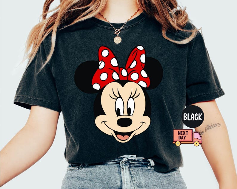 Może przedstawiać: Czarny T-shirt z grafiką Minnie Mouse w czerwonej kokardce w białe kropki. Koszulka ma postarzony wygląd.