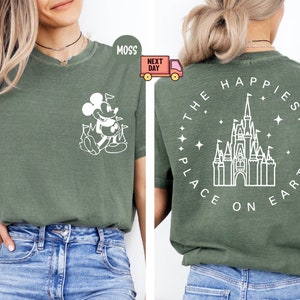 K&ouml;nnte beinhalten: Ein gr&uuml;nes T-Shirt mit einer wei&szlig;en Umrandung von Mickey Mouse auf der Vorderseite und einer wei&szlig;en Umrandung von Schloss Aschenputtel mit dem Text "The Happiest Place on Earth" auf der R&uuml;ckseite.