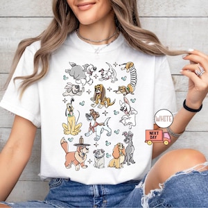 May include: White t-shirt featuring a colorful cartoon illustration of various dog breeds. The design includes dogs of different sizes and colors, with a playful and whimsical style. The shirt has a round neckline and short sleeves.