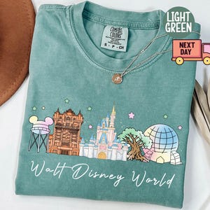 May include: Light green t-shirt with a Walt Disney World graphic. The design includes a water tower, Hollywood Tower, Cinderella Castle, and a Spaceship Earth illustration. The words "Walt Disney World" are written in cursive.
