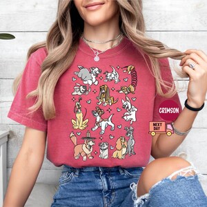 May include: A red t-shirt featuring a collection of cartoon dogs in various poses. The dogs are in different colors and breeds, with hearts and stars scattered around them. The shirt has the text "CRIMSON" and "NEXT DAY" on it.