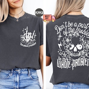 Könnte beinhalten: Ein dunkelgraues T-Shirt mit einem weißen Totenkopf und einem Blumendesign auf der Rückseite. Der Text auf der Rückseite lautet "Don't be a part of the problem be the whole problem". Die Vorderseite des Shirts hat eine weiße Skeletthand mit dem Text "the whole problem".