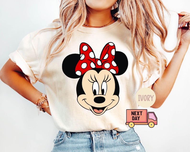 Może przedstawiać: Biały t-shirt z czerwono-białym rysunkiem animowanym Minnie Mouse w czerwonej kokardce w białe kropki. Na zdjęciu widoczny jest tekst "IVORY" i "NEXT DAY".