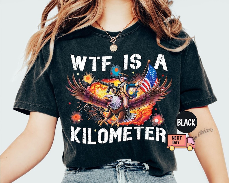 May include: Black graphic t-shirt with the text "WTF IS A KILOMETER". The design features an eagle carrying a person with a gun and an American flag, set against a fiery background.