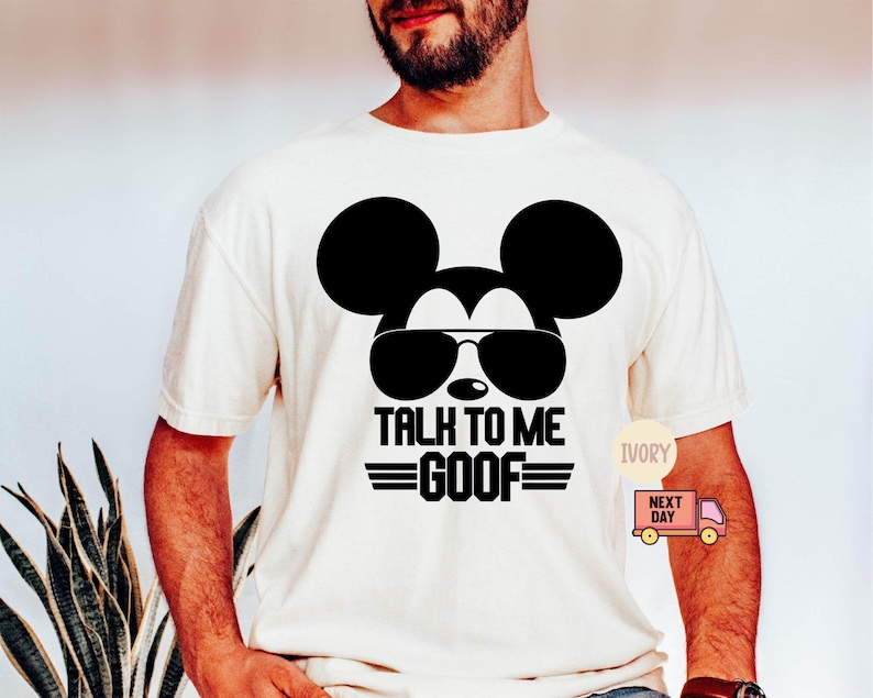 May include: An ivory short-sleeved t-shirt featuring a black graphic of a mouse silhouette wearing sunglasses. Below the graphic, the text reads TALK TO ME GOOF in bold black capital letters, flanked by two horizontal lines on each side of the word GOOF.