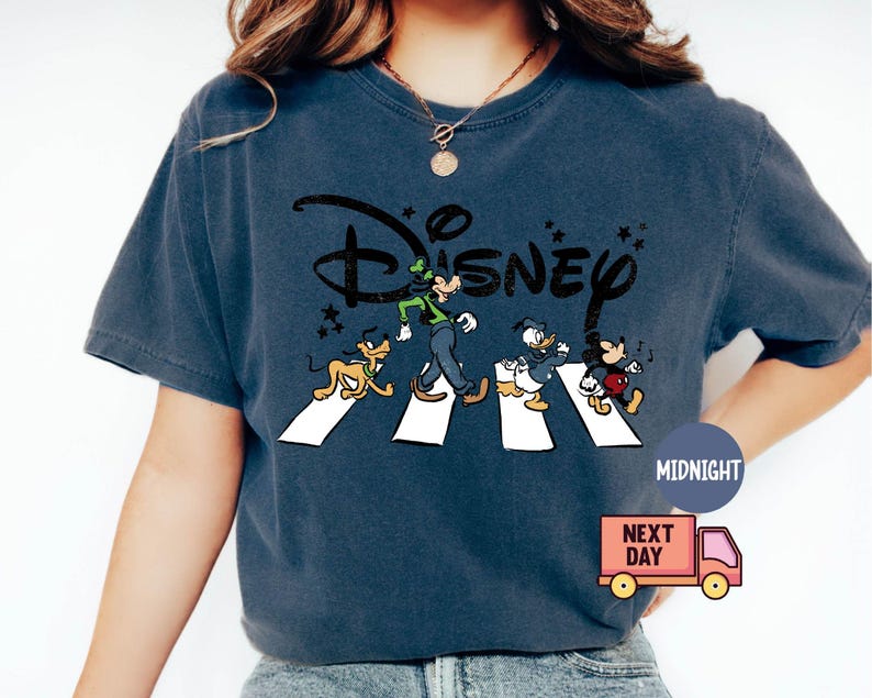 K&ouml;nnte beinhalten: Marineblaues T-Shirt mit einem Disney-Design mit Goofy, Pluto, Donald Duck und Mickey Mouse, die eine Stra&szlig;e &uuml;berqueren. Das Disney-Logo befindet sich &uuml;ber den Figuren. Das T-Shirt hat einen Vintage-Look.