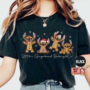 Puede incluir: Camiseta negra con un dise&ntilde;o de Stitch con tem&aacute;tica de pan de jengibre. El gr&aacute;fico incluye cuatro personajes de Stitch decorados como hombres de jengibre, con el texto "Stitch's Gingerbread Baking & Co" debajo. La camiseta tiene un corte holgado.