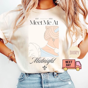 以下が含まれることがあります： 「Meet Me At Midnight」の文字と女性の横顔のイラストが描かれたアイボリー色のTシャツ。「EST 1950」の文字と小さなフルール・ド・リスのシンボルも特徴です。ピンク色の配達トラックのグラフィックも表示されています。
