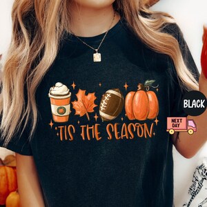May include: Black t-shirt with a graphic design featuring a pumpkin, football, coffee cup, and a leaf. The text "Tis the season" is printed below the graphic.