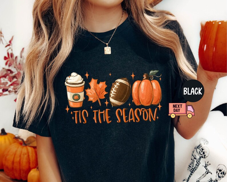 May include: Black t-shirt with a graphic design featuring a pumpkin, football, coffee cup, and a leaf. The text "Tis the season" is printed below the graphic.