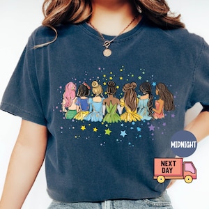 Puede incluir: Una camiseta azul marino con un gr&aacute;fico de siete princesas sentadas juntas con estrellas en el fondo. Las princesas llevan vestidos coloridos y tienen el pelo largo. El texto "MIDNIGHT" est&aacute; en la esquina inferior derecha de la camiseta.