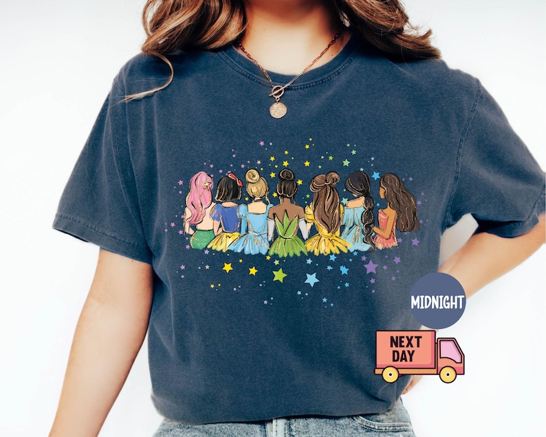 Puede incluir: Una camiseta azul marino con un gr&aacute;fico de siete princesas sentadas juntas con estrellas en el fondo. Las princesas llevan vestidos coloridos y tienen el pelo largo. El texto "MIDNIGHT" est&aacute; en la esquina inferior derecha de la camiseta.