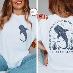 Op de afbeelding: Wit T-shirt met een blauwe walvishaai-afbeelding en de tekst "Wanneer je door diep water gaat, ben ik bij je. Jesaja 43:2"