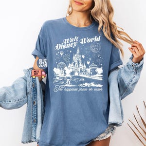 May include: Blue t-shirt with a white graphic of Cinderella's castle and fireworks, with the text "Walt Disney World" and "The happiest place on earth". The shirt has rolled-up sleeves.