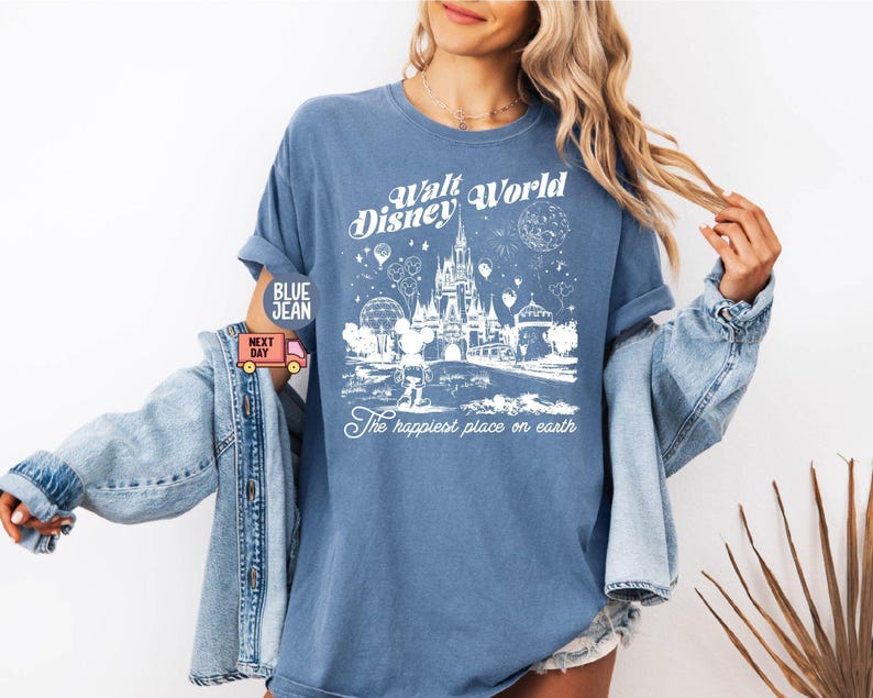 May include: Blue t-shirt with a white graphic of Cinderella's castle and fireworks, with the text "Walt Disney World" and "The happiest place on earth". The shirt has rolled-up sleeves.