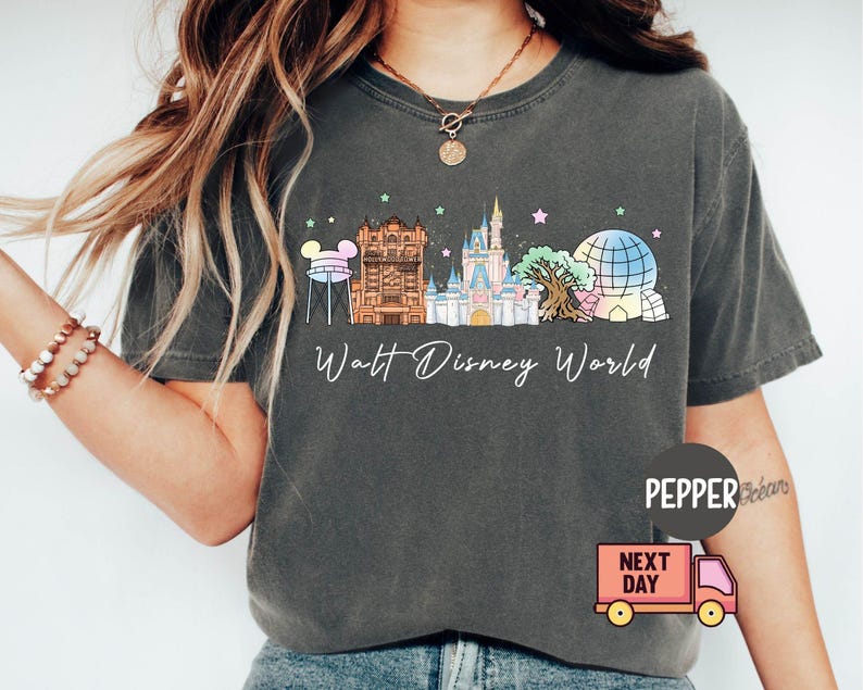 May include: Dark gray t-shirt featuring a colorful illustration of the Walt Disney World skyline. The design includes iconic landmarks like Cinderella Castle and Spaceship Earth, with the words "Walt Disney World" in a script font.