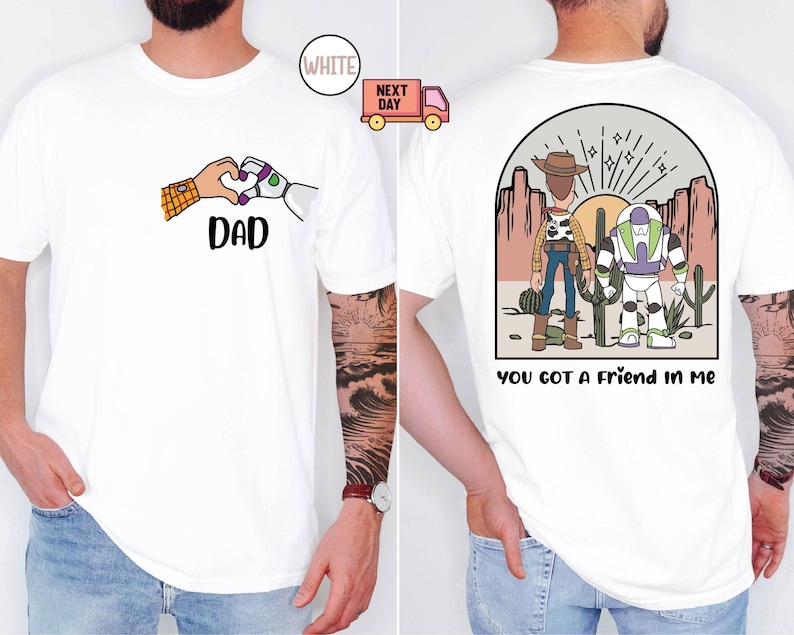Pu&ograve; includere: Una t-shirt bianca con una grafica frontale di una mano umana e una mano robotica che formano un cuore sopra la scritta DAD. La grafica sul retro mostra due personaggi dei cartoni animati in un deserto con la scritta YOU GOT A FRIEND IN ME.